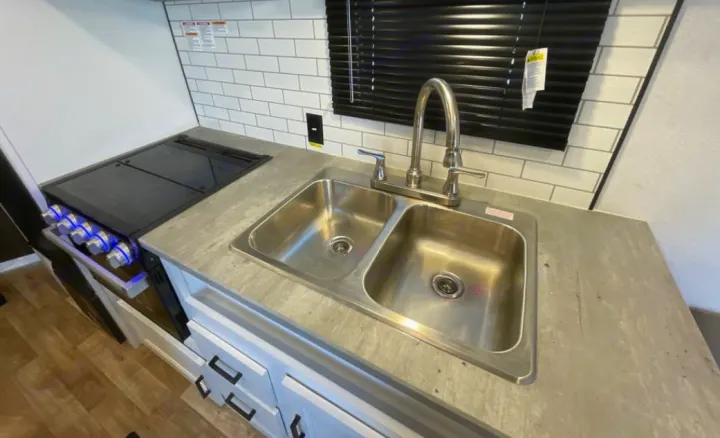 Clean RV rental kitchen interior featuring a dual sink, stove with blue lights, and subway tile backsplash.. Keystone RV Hideout 2023