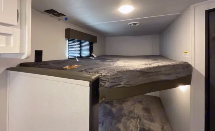 Cozy bunk beds inside an RV rental, with a soft grey top bunk and bright interior lighting.. Keystone RV Hideout 2023