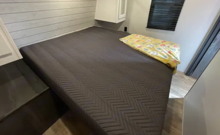 Cozy RV rental bedroom with a dark grey bed, yellow blanket, and light wood interior. Ideal for travel accommodation.. Keystone RV Hideout 2023