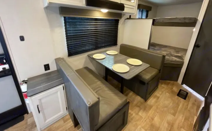 Interior of a modern rv rental showing a dinette with table and plates, window, and bunk beds.. Keystone RV Hideout 2023