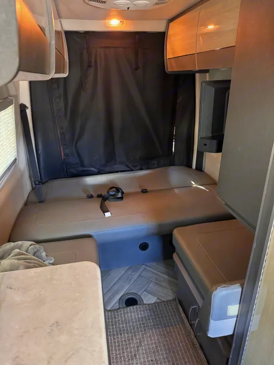 Cozy RV rental interior with convertible dinette/bed, overhead storage, and integrated fridge.. Thor Sanctuary 2024