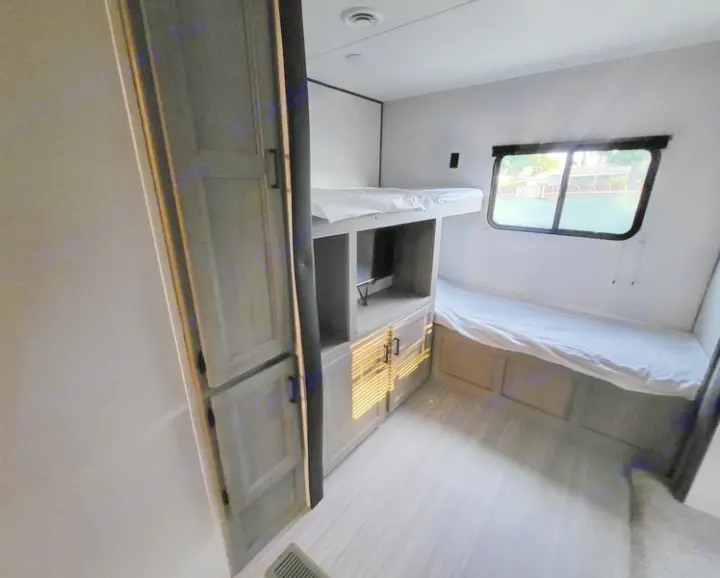 Inside an RV rental: a bright bunkhouse area with two beds, light wood storage, and a large window view.. Keystone Hideout 2021