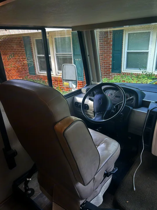 Inside an RV rental: a clear view of the driver's seat, dashboard, and a house visible through the windshield.. Winnebago Intent 2018