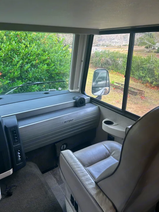 Step inside this RV rental's spacious cockpit. Enjoy comfortable seating, the dashboard with 'INTENT' text, and a vibrant outdoor view.. Winnebago Intent 2018
