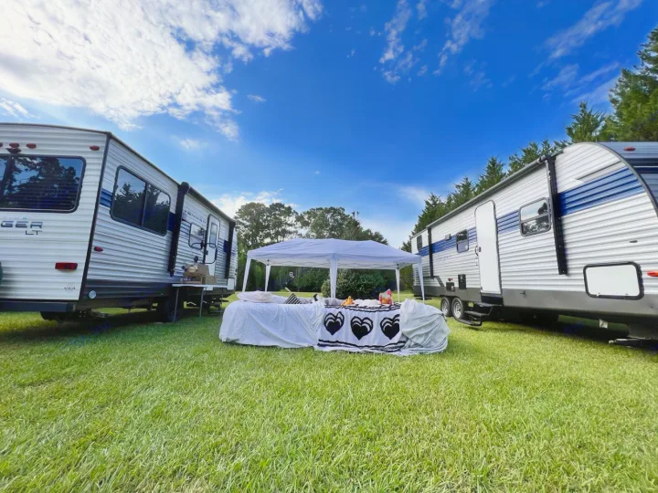 Enjoy an RV rental experience: Two travel trailers flank a tent and decorated table on a sunny lawn.. Avenger LE 2022