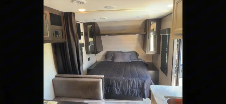 Explore this RV rental's inviting interior: a compact bedroom featuring a comfortable bed, storage, and control panel.. Jayco Jay Flight SLX 2022