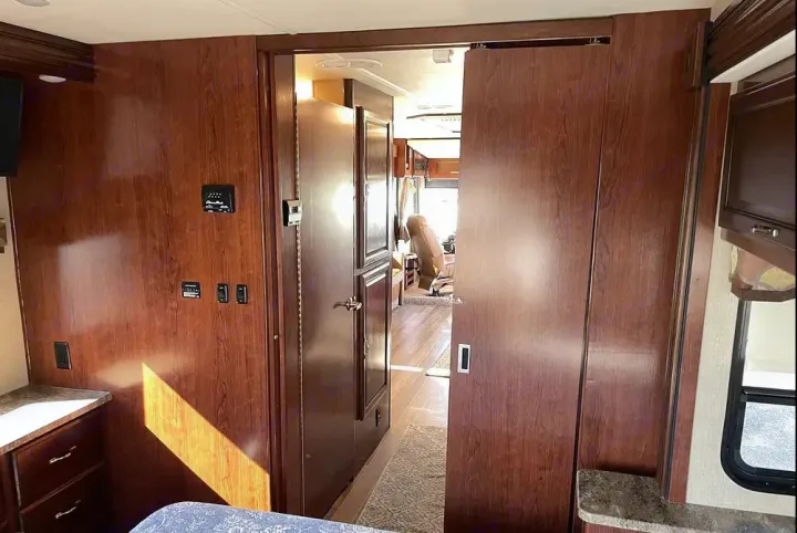 Cozy RV rental interior: wood-paneled bedroom area, hallway, and open sliding doors leading to the front living space.. Flair-Fleetwood LXE 2018