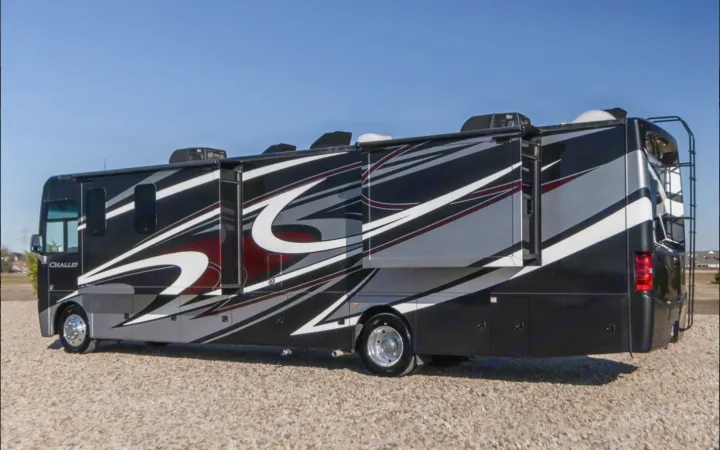 Large black & grey RV rental motorhome with extended slides, parked on gravel under a clear sky.. Thor Challenger 2021