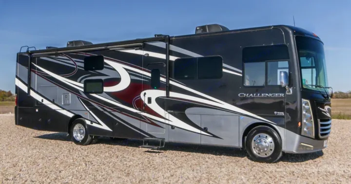 A sleek black and grey Class A motorhome with dynamic white and burgundy graphics, ideal for your next RV rental adventure, parked on gravel.. Thor Challenger 2021