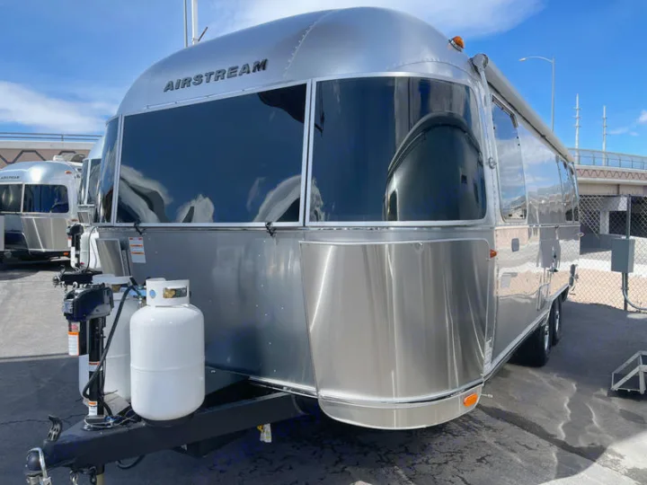 Shiny Airstream rv rental travel trailer parked outdoors. Large front windows, propane tanks visible.. Airstream Globetrotter 2024