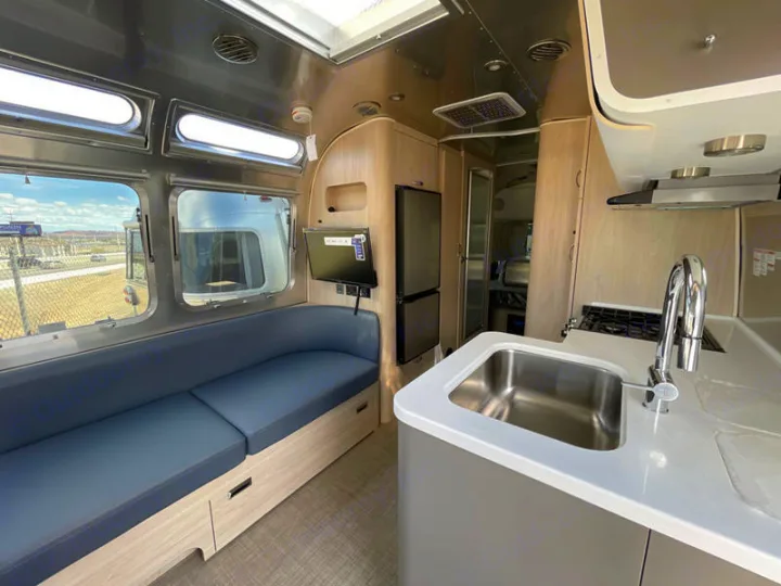 Step inside this modern RV rental featuring a comfortable living area with a sofa, TV, and a functional kitchen.. Airstream Globetrotter 2024