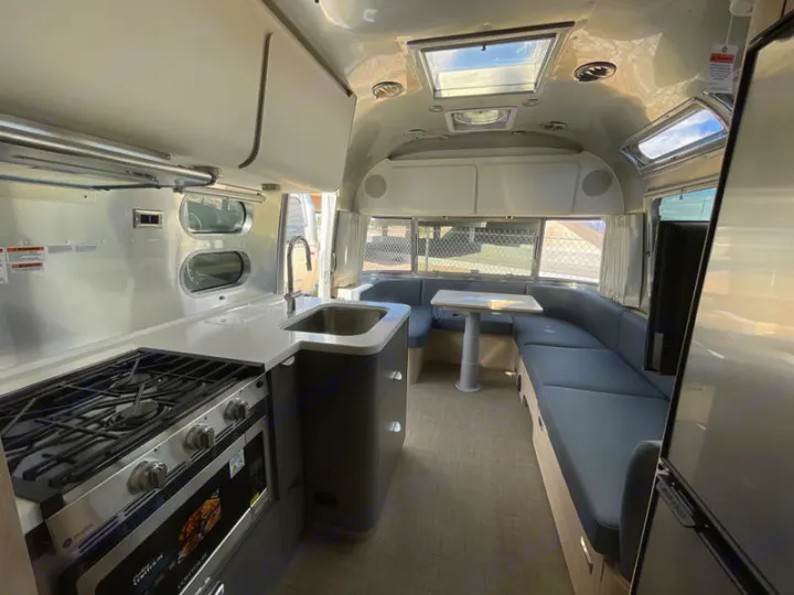 Inside a sleek rv rental: a compact kitchen with stove and sink, plus a comfy U-shaped dining lounge.. Airstream Globetrotter 2024