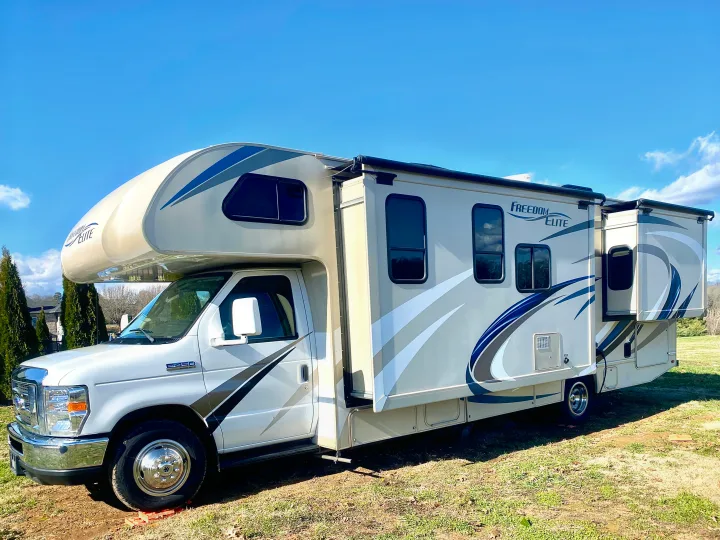 This Freedom Elite rv rental is a white & beige Class C motorhome parked on grass with slides extended, ready for adventures.. Thor Freedom Elite 2018