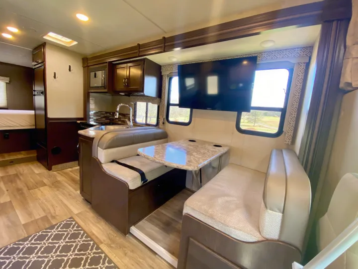 Comfortable RV rental interior with dinette, kitchen, TV, and wood-look flooring. Ideal for travel adventures.. Thor Freedom Elite 2018