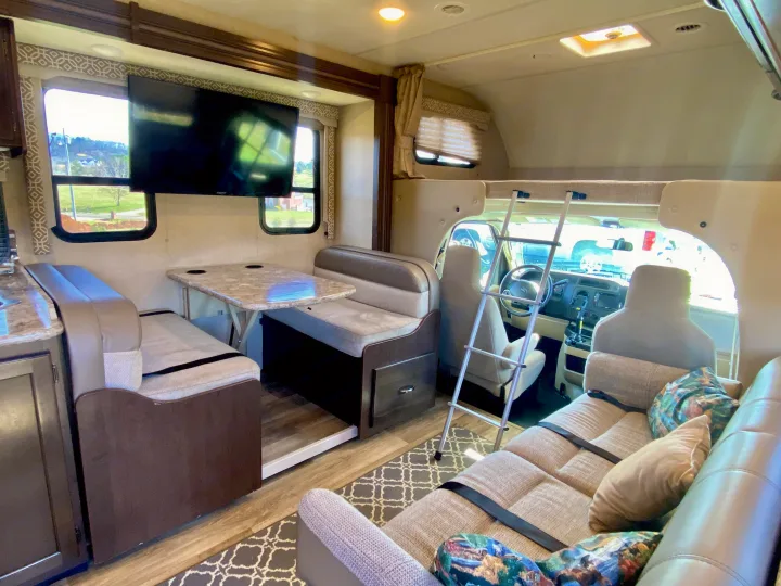 Spacious rv rental interior featuring a dinette, kitchen, over-cab bed, and front cockpit, ready for your road trip.. Thor Freedom Elite 2018