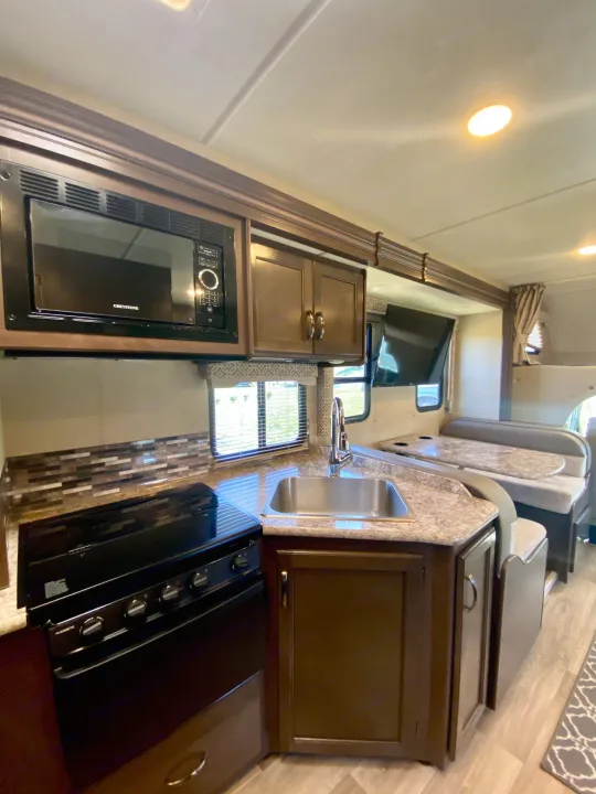 Inside an RV rental: full kitchen with microwave, stove, sink, and dining area with a booth and table.. Thor Freedom Elite 2018