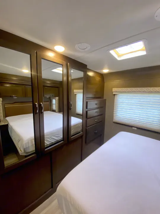 Inside an RV rental: a compact bedroom featuring two beds (one reflected), mirrored closet doors, and built-in drawer storage.. Thor Freedom Elite 2018