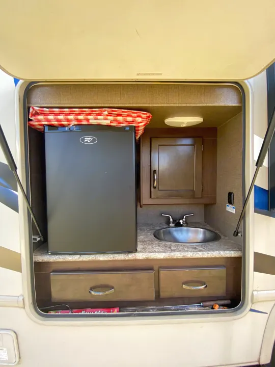 RV rental outdoor kitchen setup: mini-fridge, sink, and cabinets. Ideal for camping convenience with everything at hand.. Thor Freedom Elite 2018