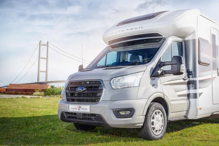 Explore with an RV rental! This grey Ford Transit Auto-Trail motorhome is parked on grass near a large suspension bridge.. Auto-Trail F74 2025