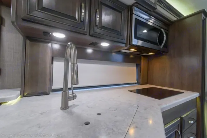 Explore comfort in this RV rental kitchen: white countertop, stainless faucet, microwave, and induction cooktop.. Entegra Coach Accolade 2023