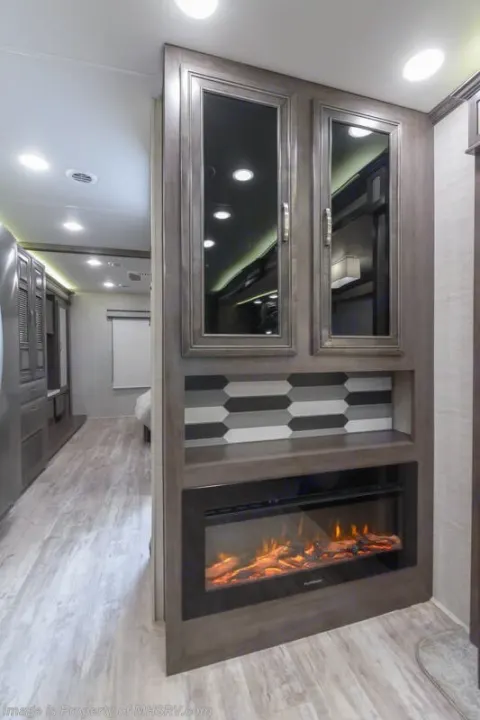 Stylish RV rental interior showcasing a cozy electric fireplace, glass-front cabinets, and modern tile.. Entegra Coach Accolade 2023