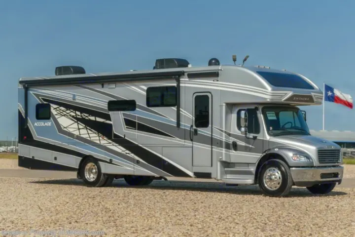 Sleek grey Entegra Accolade RV for rv rental, featuring bold graphics. Parked on gravel with a Texas flag nearby.. Entegra Coach Accolade 2023