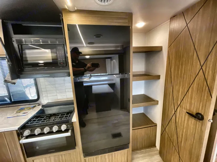 Modern RV rental: a kitchen with microwave, stove, large black fridge, and open storage shelves visible.. Forest River Salem 2025