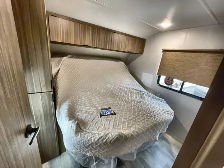 Spacious RV rental bedroom featuring a comfy king bed, overhead cabinets, and window with shade for restful travel.. Forest River Salem 2025