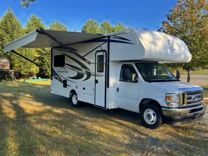 White Nexus Phantom RV rental with extended awning, parked on grass. This motorhome is ready for your next outdoor adventure.. Nexus Phantom 2025