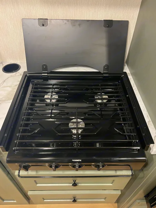This Dometic three-burner gas range in an RV rental features a sleek black finish, open hinged cover, and control knobs.. Nexus Phantom 2025