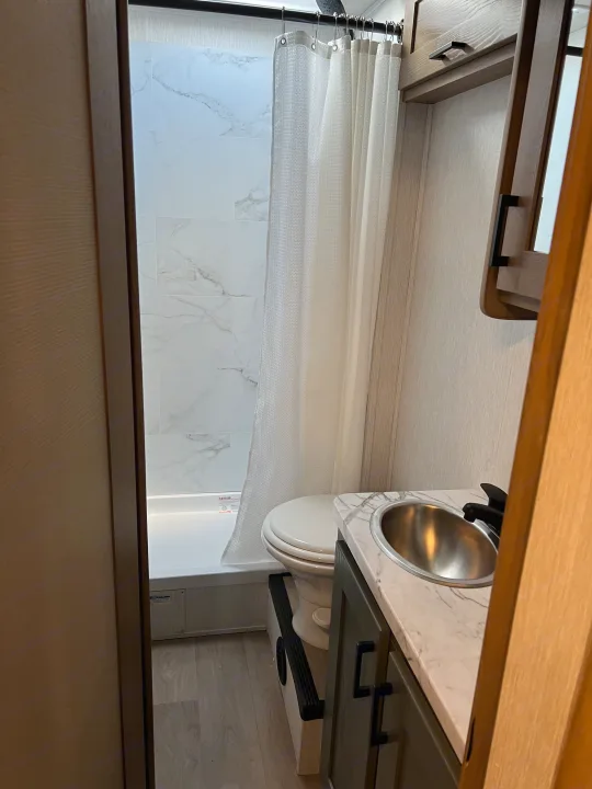 Explore this compact RV rental bathroom featuring a marble-look tiled shower, toilet, and modern vanity with sink.. Nexus Phantom 2025
