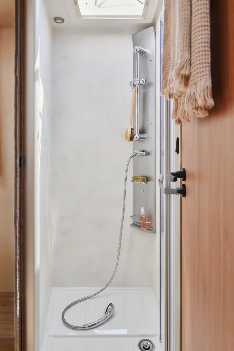 Clean, compact RV rental shower unit with modern fixtures, including a handheld showerhead, soap, and hanging brush.. Pilote G740FC EVIDENCE 2025