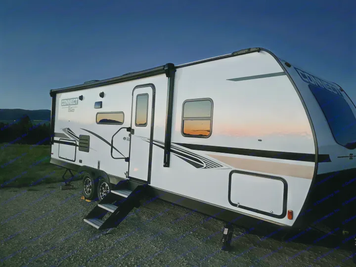 Golden sunset reflections on a white travel trailer, parked under a darkening sky. Ideal for an RV rental getaway.. Connect SE 2022