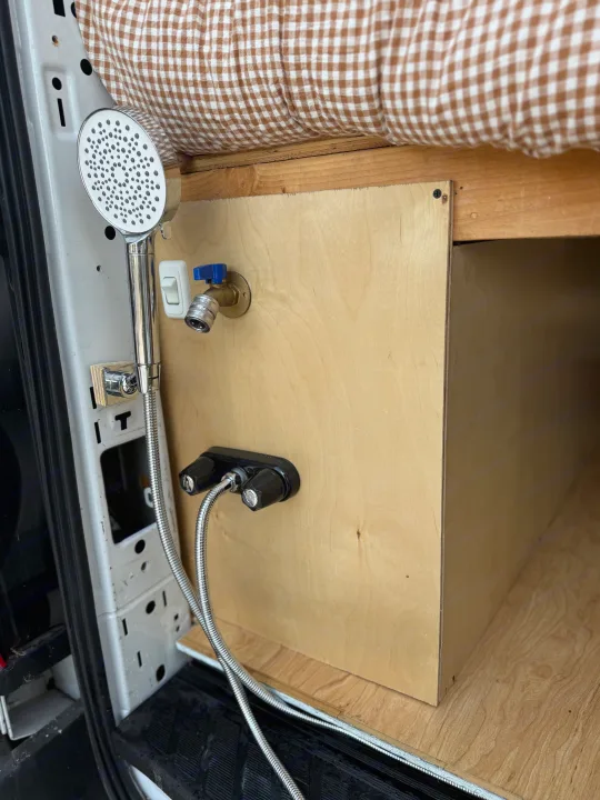 Compact RV rental shower setup: handheld shower, hot/cold mixer, and quick-connect spigot in van interior.. Ford Transit 2021
