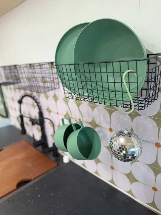 Compact RV rental kitchen storage: green plates, cups, & a fun disco ball hang on a patterned backsplash.. Ford Transit 2021