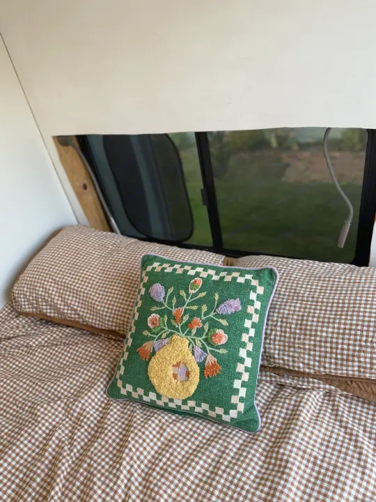 Cozy RV rental interior with brown gingham bedding and a green, floral embroidered pillow by the window.. Ford Transit 2021