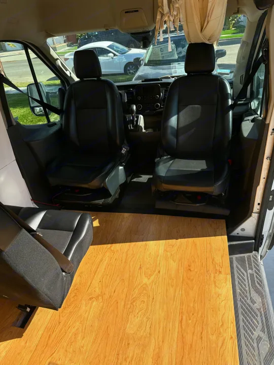 RV rental van interior: black front seats, dash, light wood floor extending to rear seating.. Ford Transit 2021