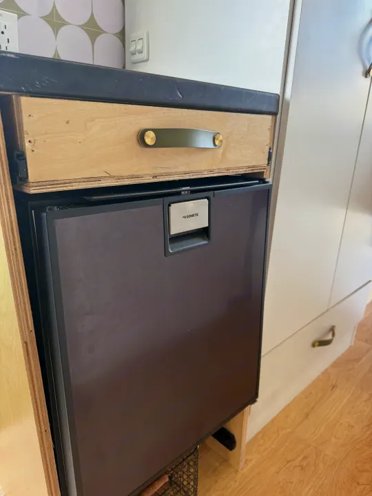 Inside this RV rental: a Dometic refrigerator, a wooden drawer with a distinctive green and brass handle, and light cabinetry.. Ford Transit 2021