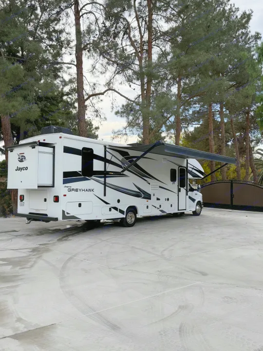 Spacious Jayco Greyhawk RV rental with slide-out & awning, parked on concrete amid tall pines.. Jayco Greyhawk 2023