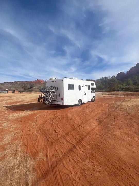 White RV rental with bike rack parked on red dirt, under blue sky amidst scenic desert mountains.. Thor Majestic 2019