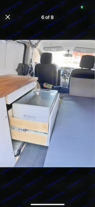 RV rental interior: custom camper van featuring a slide-out fridge, wooden countertop, and comfy bed.. Nissan NV200 2015