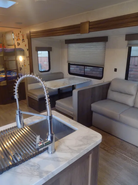 Bright RV rental interior: kitchen with sink, dining booth, sofa, and bunk beds visible.. East to West Silver Lake 2021