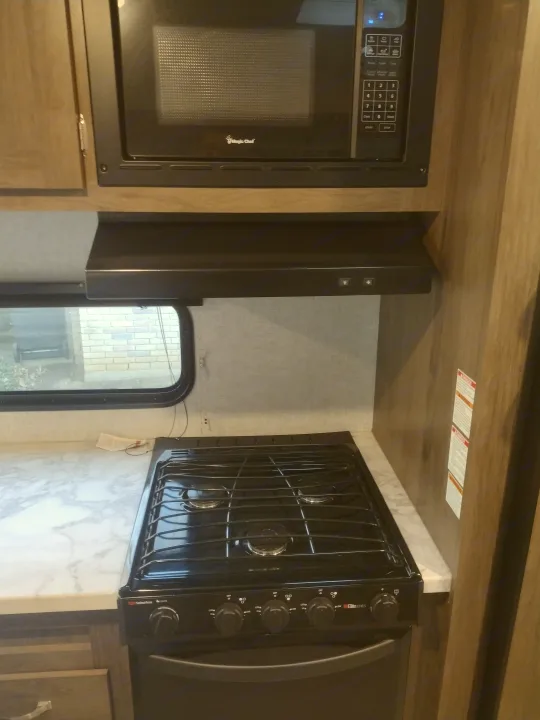 Compact kitchen in an RV rental, featuring an over-the-range microwave, gas stovetop with oven, and window.. East to West Silver Lake 2021