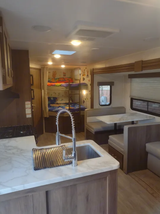 Modern RV rental interior: kitchen, dining, and cozy bunk beds with cartoon decor, perfect for family adventures.. East to West Silver Lake 2021