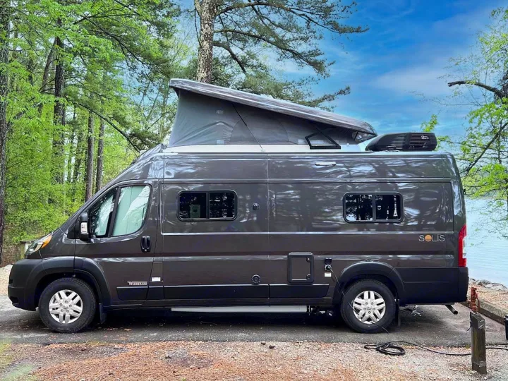 Grey Winnebago Solis pop-top RV rental parked lakeside in a lush forest campsite, ready for adventure.. Winnebago Solis 59PX 2025