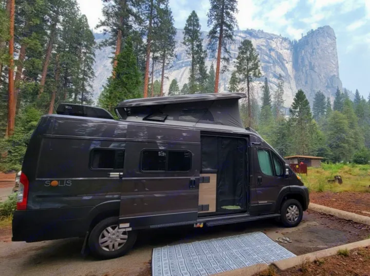 This Winnebago Solis RV rental is parked at a scenic forest campsite with a massive granite mountain backdrop, perfect for camping.. Winnebago Solis 59PX 2025