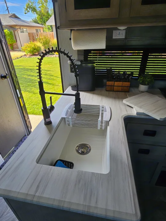 RV rental kitchen with modern sink, faucet, and coffee maker, looking out to a sunny backyard. Perfect for cooking on the go.. Forest River Salem 2024