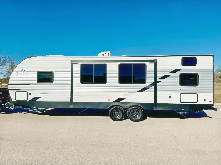 This sleek, modern white and grey travel trailer, suitable for an RV rental, is parked on asphalt under a bright blue sky.. East to West Della Terra LE 2024