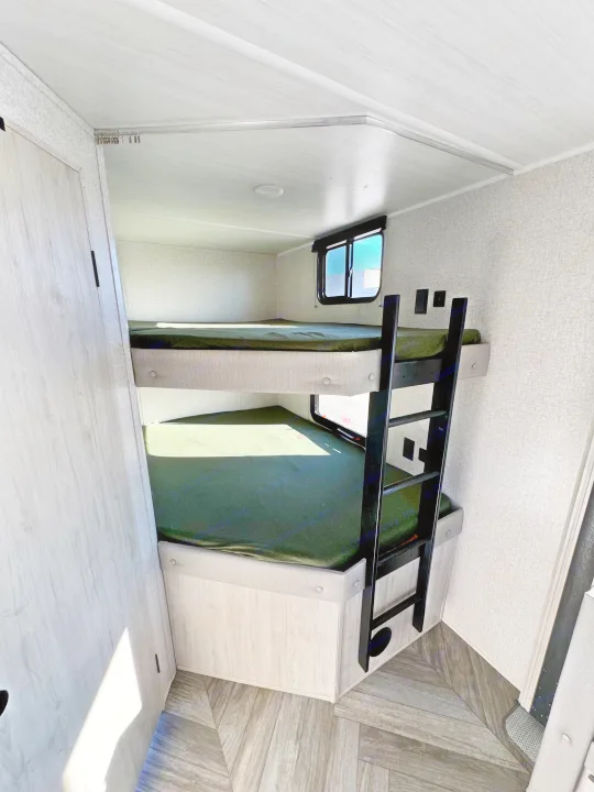 Cozy RV rental interior featuring two bunk beds with green sheets, a ladder, and a window for compact sleeping.. East to West Della Terra LE 2024