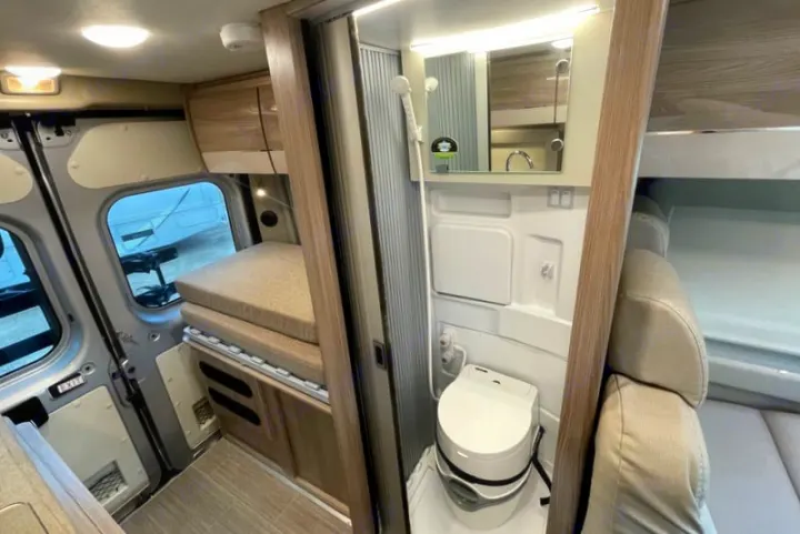 Compact RV rental interior featuring a wet bath with toilet and shower, next to a convertible bed/seating area.. Thor Scope 2023